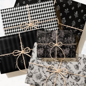 May include: An assortment of wrapped gifts with various black and white patterned papers. Designs include floral, diamond, and striped patterns. Each package is tied with twine bows, creating a rustic and elegant presentation. The gifts are arranged on a white surface.