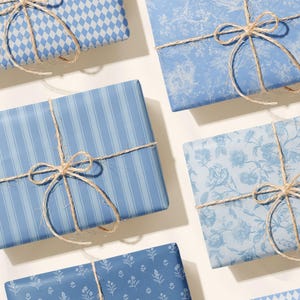 May include: Several wrapped gifts with blue patterned paper and twine bows. The patterns include stripes, floral, and diamond shapes. The gifts are arranged on a white surface, creating a visually appealing presentation.