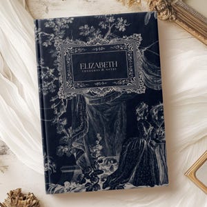 May include: A black journal with a silver floral design and the text "ELIZABETH THOUGHTS & NOTES" on the front cover.