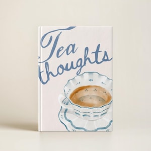 May include: A white journal with the text "Tea Thoughts" in blue script. The cover features a watercolor illustration of a white teacup and saucer with blue trim and brown tea.