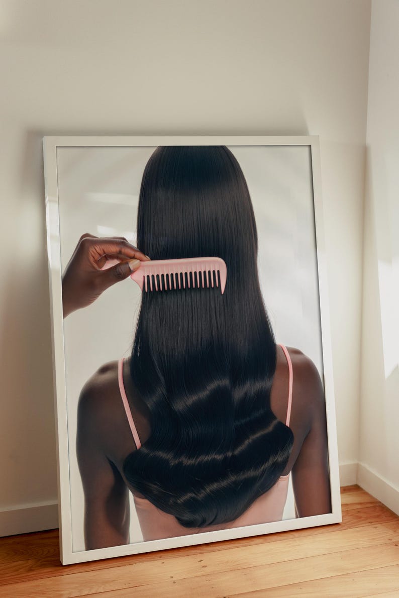May include: A framed image featuring a person with long, dark hair being combed with a pink comb. The person is wearing a pink top. The image is set against a white background and rests on a wooden floor.