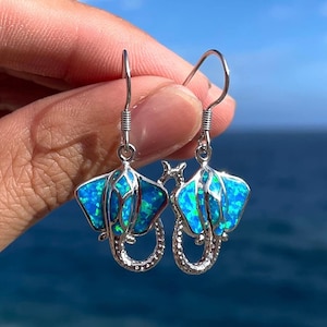 Op de afbeelding: Oorbellen van sterling zilver met een ontwerp van een blauwe opaal-rog. De oorbellen zijn van het hangende type met een haaksluiting.