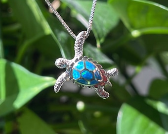 May include: A silver necklace with a blue opal turtle pendant. The turtle is facing the right side of the image.