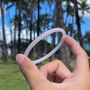 May include: A white plastic ring held in a hand against a background of palm trees and a blue sky.