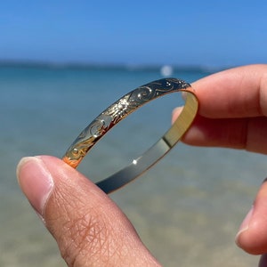 Op de afbeelding: Een gouden armband met een bloemenpatroon.