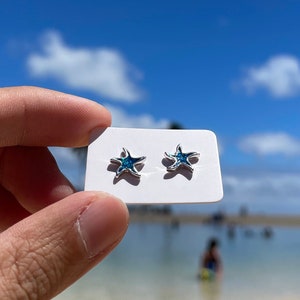 May include: A pair of silver starfish earrings with blue gemstones on a white card.
