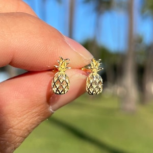 Op de afbeelding: Een paar gouden ananas oorbel studs. De oorbellen zijn klein en delicaat, en ze zijn perfect om een ​​tropische touch toe te voegen aan elke outfit.