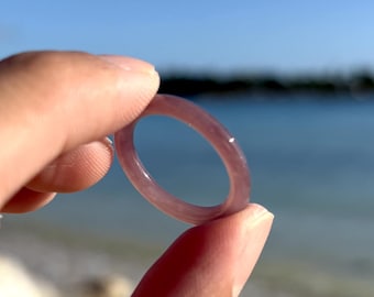 May include: A translucent purple ring made of glass or plastic, held up against a background of a beach and ocean.