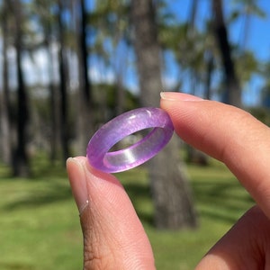 May include: A purple resin ring with a sparkly finish. The ring is shown on a finger against a blurred background of palm trees.