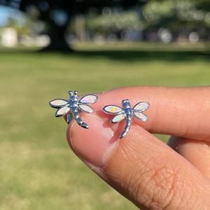 May include: A pair of silver dragonfly earrings with white opal accents. The earrings are small and delicate, perfect for everyday wear.