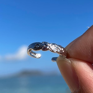 May include: A silver toe ring with a delicate floral design. The ring is open and adjustable to fit most toe sizes.