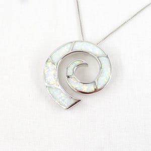 May include: A silver-toned spiral pendant necklace featuring inlaid white opal segments. The pendant has a curved, open-ended circular design with a polished metal frame, suspended from a thin, delicate silver-toned chain.
