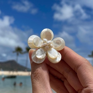 Puede incluir: Un broche blanco en forma de flor hecho de nácar con un grupo de perlas blancas en el centro.