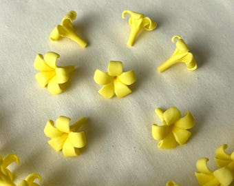 May include: Bright yellow floral embellishments, including individual flowers and a connected garland, are scattered on a cream-colored surface. The flowers have a delicate, detailed design, with petals and a trumpet-like shape. The overall theme is floral and decorative.