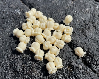 May include: A pile of white ceramic beads with a flower-like design. The beads are arranged in a random pattern on a dark gray surface.