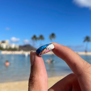 May include: A silver ring with a multi-colored opal inlay. The opal is a mix of blue, pink, and white.