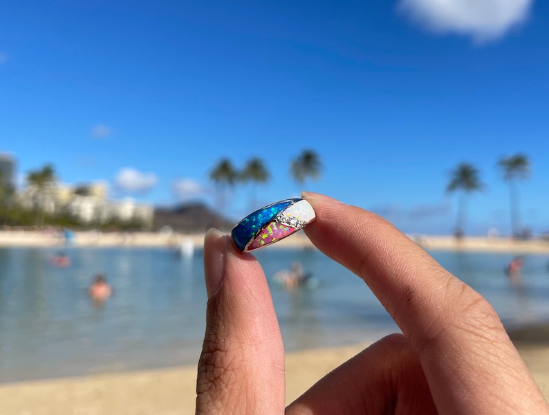 May include: A silver ring with a multi-colored opal inlay. The opal is a mix of blue, pink, and white.