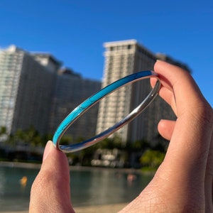 May include: A silver bangle bracelet with a turquoise inlay. The bracelet is thin and delicate, and the turquoise inlay is a light blue colour.