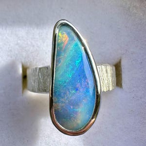 May include: A silver ring featuring a blue opal gemstone set in a silver bezel. The opal is teardrop shaped and is surrounded by a silver band.