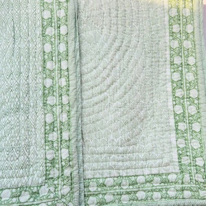 May include: A green and white cotton quilt with a leaf pattern. The quilt has a decorative border with a floral design.