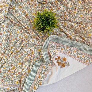 Op de afbeelding: Een wit katoenen dekbed met een bloemenprint in tinten geel, oranje en groen. Het dekbed heeft een groene en witte rand met een gestreept patroon.