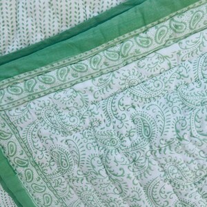 Könnte beinhalten: Eine weiß-grüne Steppdecke mit Paisley-Muster und grünem Rand. Die Steppdecke hat ein sich wiederholendes Paisley-Design in hellgrüner Farbe. Der Rand ist einfarbig grün. Die Steppdecke ist gefaltet und zeigt das Muster und die Textur.