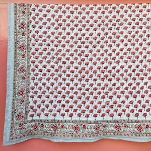Puede incluir: Una colcha de algodón blanco con un patrón floral rojo y verde. La colcha tiene un borde con un diseño floral más intrincado.