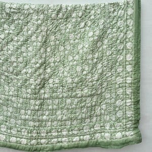 Peut inclure: Une courtepointe en coton vert avec un motif floral blanc. La courtepointe a une bordure verte et blanche.