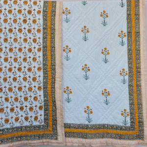 May include: A quilted textile featuring two distinct sections. The left side displays a dense pattern of small orange flowers on a white background. The right side shows a sparse floral print on a white quilted surface with a yellow border.