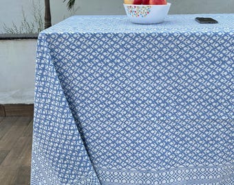 May include: A blue and white patterned tablecloth with a white border. The tablecloth is laid out on a wooden floor with a bowl of red apples on top of it.