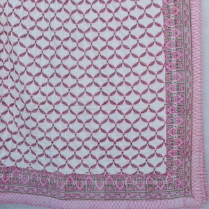 May include: A white quilt with a repeating pattern of pink leaf-like shapes. The quilt has a pink border with a decorative design and a striped edge. The overall design is symmetrical and the quilt appears to be made of a soft material.