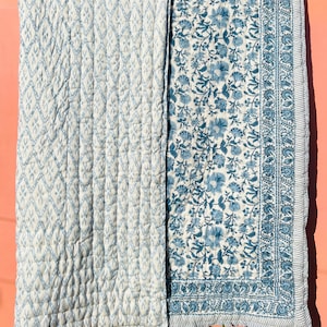 May include: A blue and white cotton quilt with a diamond pattern on one side and a floral pattern on the other side.