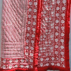 Op de afbeelding: Een rood-witte quilt met een bloemenpatroon en geometrisch ontwerp. De quilt heeft een rode rand en is gemaakt van zachte stof. Het bloemenpatroon bevat witte rozen en bladeren.