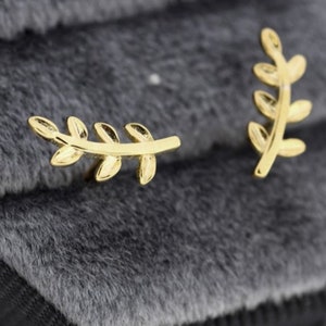 Könnte beinhalten: Ein Paar goldene Blattohrringe. Die Ohrringe sind klein und zart und haben ein schlichtes Design.