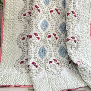Pode incluir: Uma colcha de algodão branco com estampa floral em tons de verde, azul e rosa. A colcha tem um padrão chevron na borda e uma bainha rosa.
