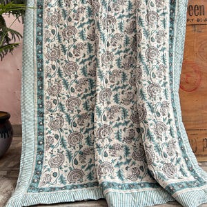 May include: A white and teal floral patterned quilt. The quilt features a repeating design of stylized flowers and leaves in teal and gray on a white background. The border has teal stripes.
