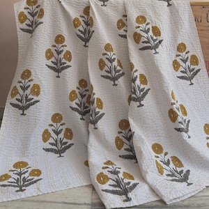 Könnte beinhalten: Weiße Baumwolldecke mit einem sich wiederholenden Blumenmuster in Senfgelb und Grau. Die Blumen haben ein stilisiertes Design und die Decke hat ein strukturiertes Aussehen. Die Decke ist gefaltet und drapiert.