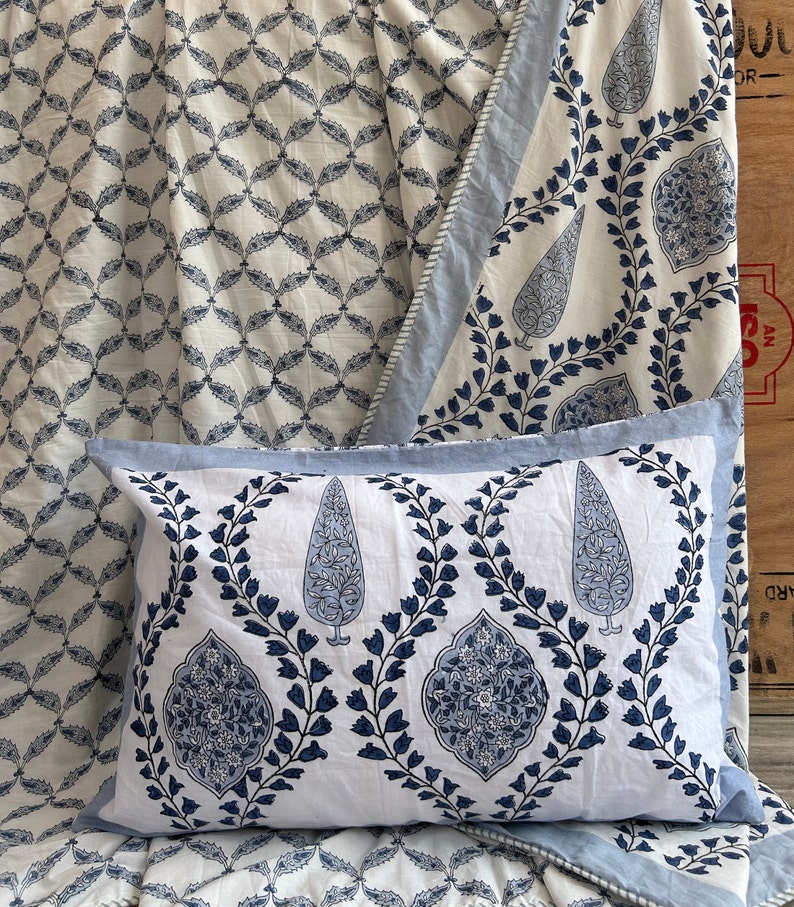 May include: A white pillow with a blue floral design and a light blue border. The pillow is part of a bedding set with matching patterned fabric in the background. The pattern includes teardrop and floral motifs.