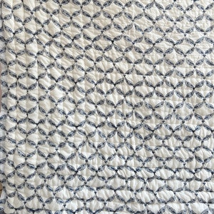 May include: White quilt with a repeating pattern of navy blue leaf-like shapes. The quilt has a quilted texture, with visible stitching creating a grid pattern across the surface. The overall design is symmetrical and visually appealing.
