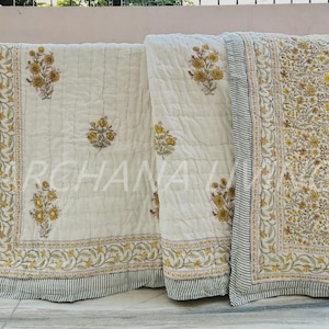 May include: Cream-coloured quilt with a floral pattern in yellow and green. The quilt features a striped border and the text "ARCHANA LIVING". The floral design is repeated across the surface.