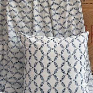 May include: A white pillow and fabric featuring a repeating pattern of navy blue leaf-like shapes. The pillow is square and rests on the fabric, which is draped in the background. The design creates a cohesive, decorative theme.