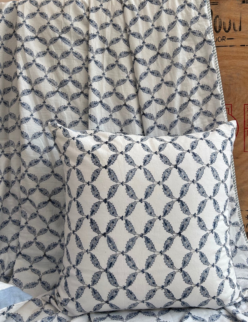 May include: A white pillow and fabric featuring a repeating pattern of navy blue leaf-like shapes. The pillow is square and rests on the fabric, which is draped in the background. The design creates a cohesive, decorative theme.