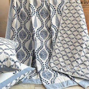 May include: A white and blue patterned quilt and matching pillow set. The quilt features a repeating design of blue floral motifs on a white background. The pillows have a similar pattern. The set is made of a soft fabric and has a light blue border.