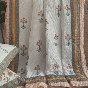 May include: A white quilted blanket and matching pillowcase featuring a repeating floral pattern with orange blossoms and green stems. The edges are framed by vertical bands of mustard yellow, teal, and a fine orange and white striped border.