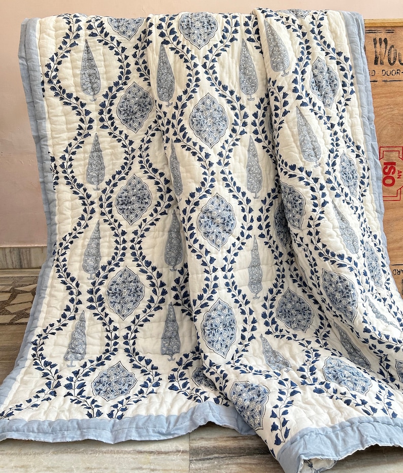 May include: A white and blue patterned quilt with a floral design. The quilt features a repeating pattern of stylized teardrop and floral shapes in shades of blue against a white background. The edges are finished with a light blue border.
