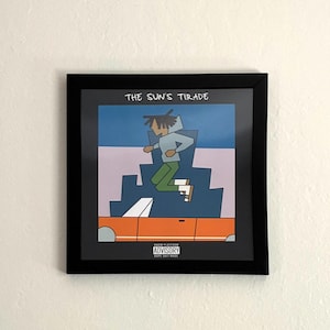 May include: A square black frame containing a print titled THE SUN'S TIRADE. The artwork features a stylized figure with dreadlocks jumping above an orange convertible car against a blue and light purple background, with a parental advisory label.