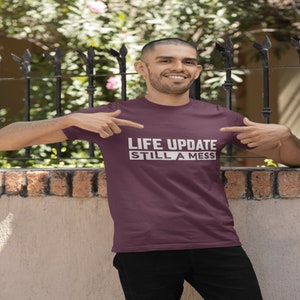 May include: A maroon t-shirt with white text that reads "LIFE UPDATE STILL A MESS".