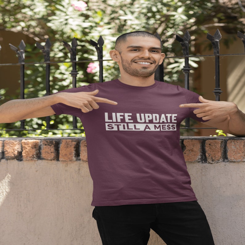 May include: A maroon t-shirt with white text that reads "LIFE UPDATE STILL A MESS".