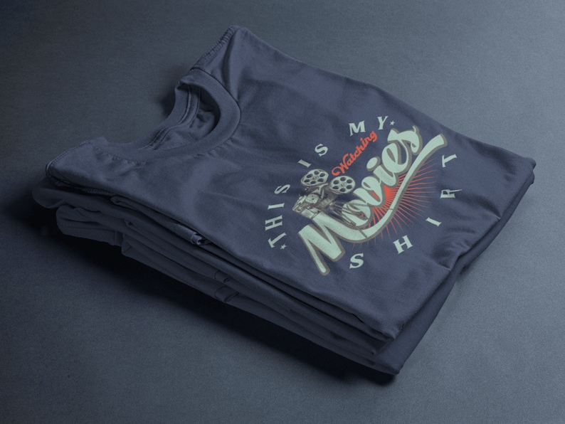 May include: A stack of navy blue t-shirts with a vintage-style graphic that says "This is my watching movies shirt".
