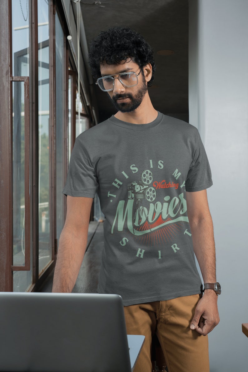 May include: A dark grey t-shirt with a vintage-style graphic of a movie projector and the text "This is my watching movies shirt".